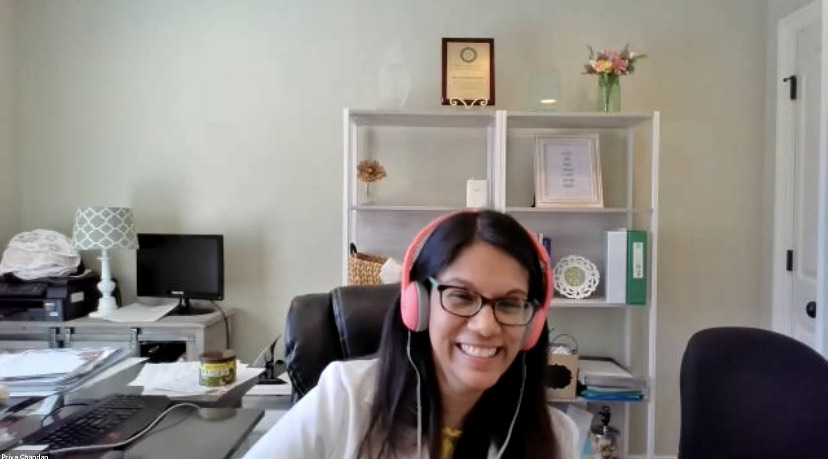 Dr. Priya Chandan Smiles at the camera. She is wearing her white Dr. coat and pink headphones.
