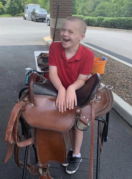 boy with down syndrome smiling and leaning on horse saddle 